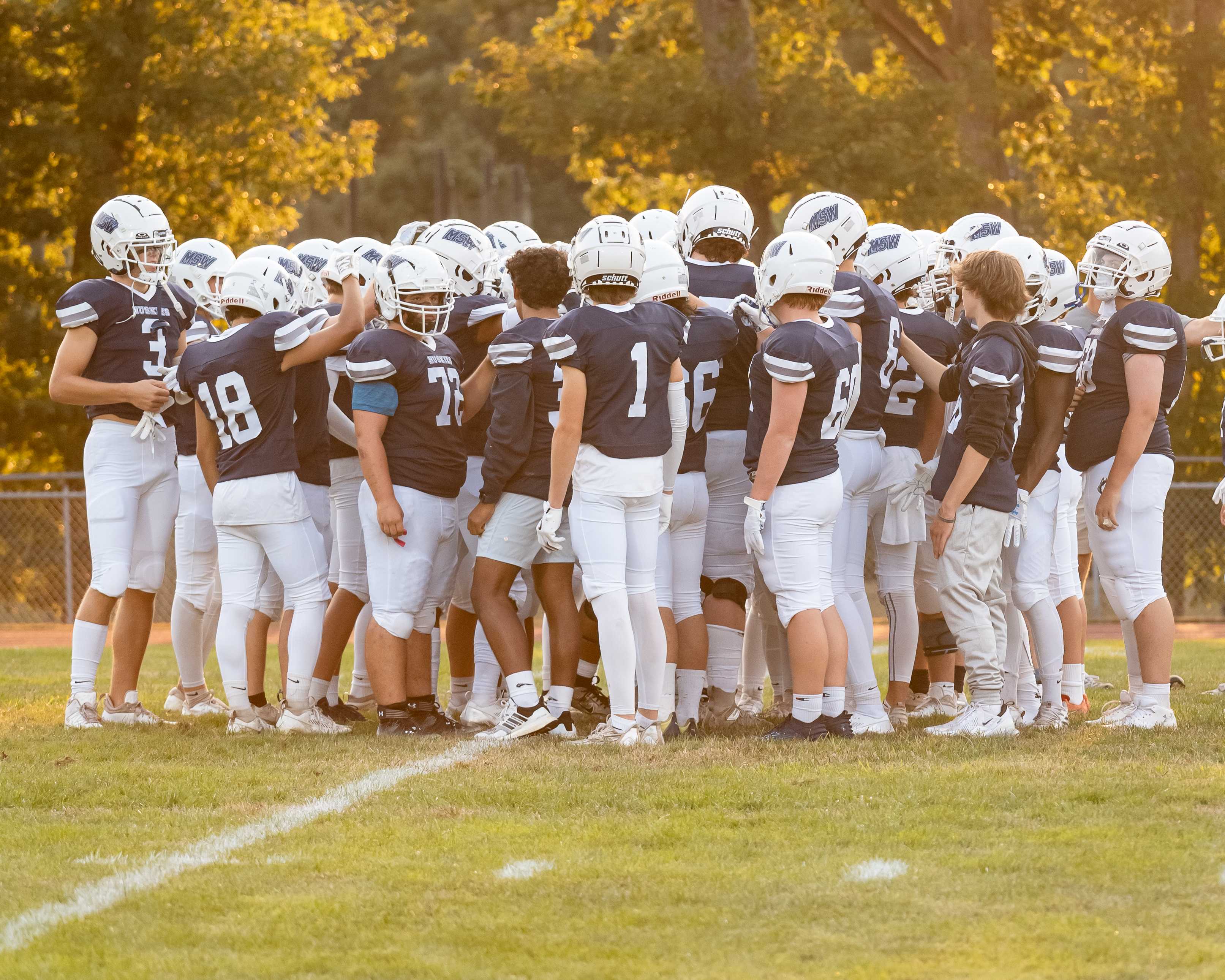 A high school football team huddles together on the field during a game.